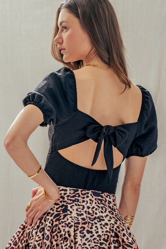 Turn heads in the Midnight Muse Bodysuit. Featuring a dramatic open back, statement bow tie, and puff sleeves, this chic black bodysuit is perfect for date night or girls’ night out.